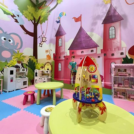 فندق إيفرجرين لوريل، تايتشونج تايتشونغ المظهر الخارجي الصورة The photo shows a colorful children's playroom designed with a whimsical theme. The walls are painted in bright colors and feature a cartoon-style mural of a pink castle with purple towers and a smiling cartoon elephant. The room is filled with playf