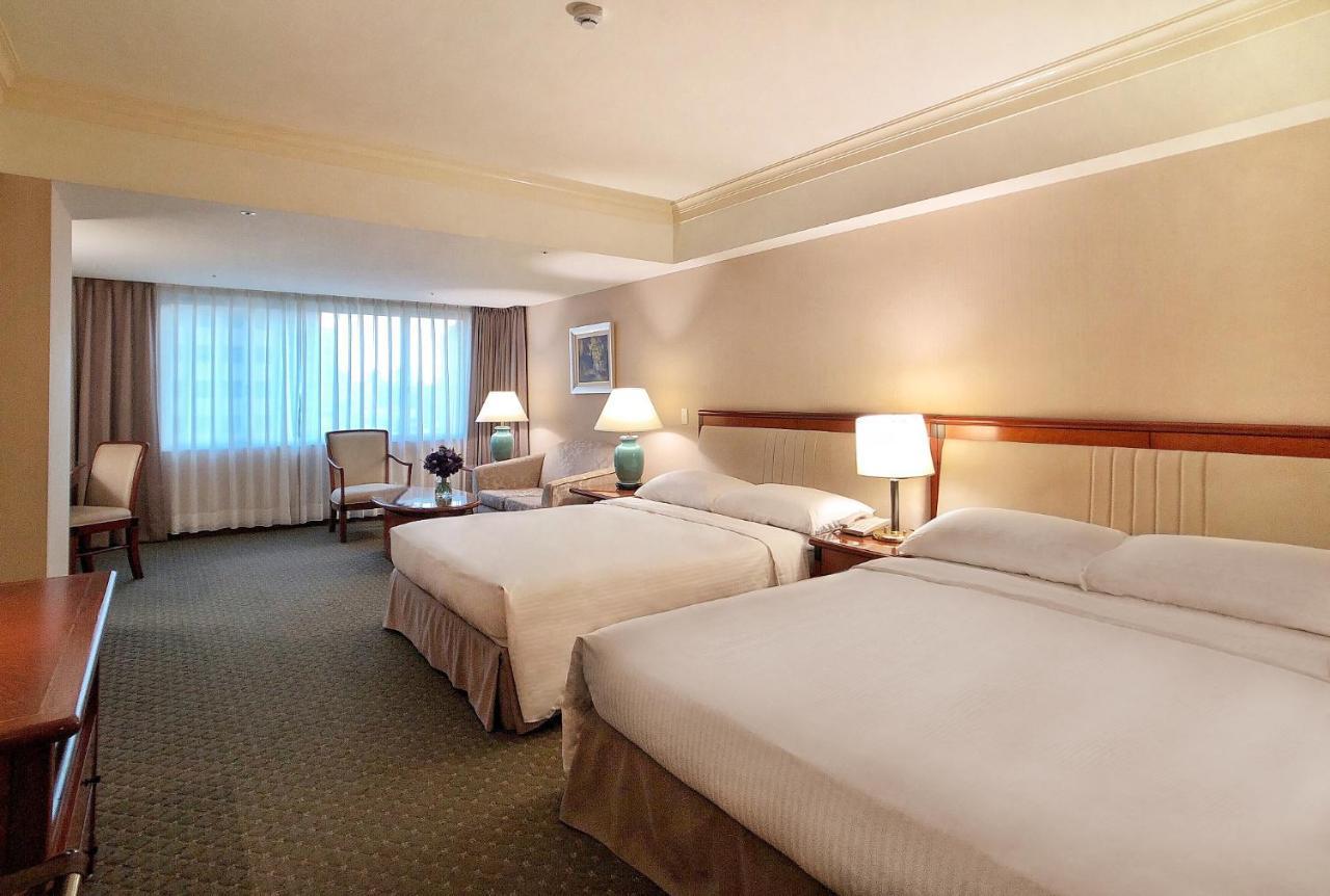 فندق إيفرجرين لوريل، تايتشونج تايتشونغ المظهر الخارجي الصورة The photo shows a hotel room featuring two queen-sized beds with white linens. The room is well-lit and has a warm, neutral color palette. There are bedside lamps on each side of the beds and a small table. To the side, there's a comfortable armchair