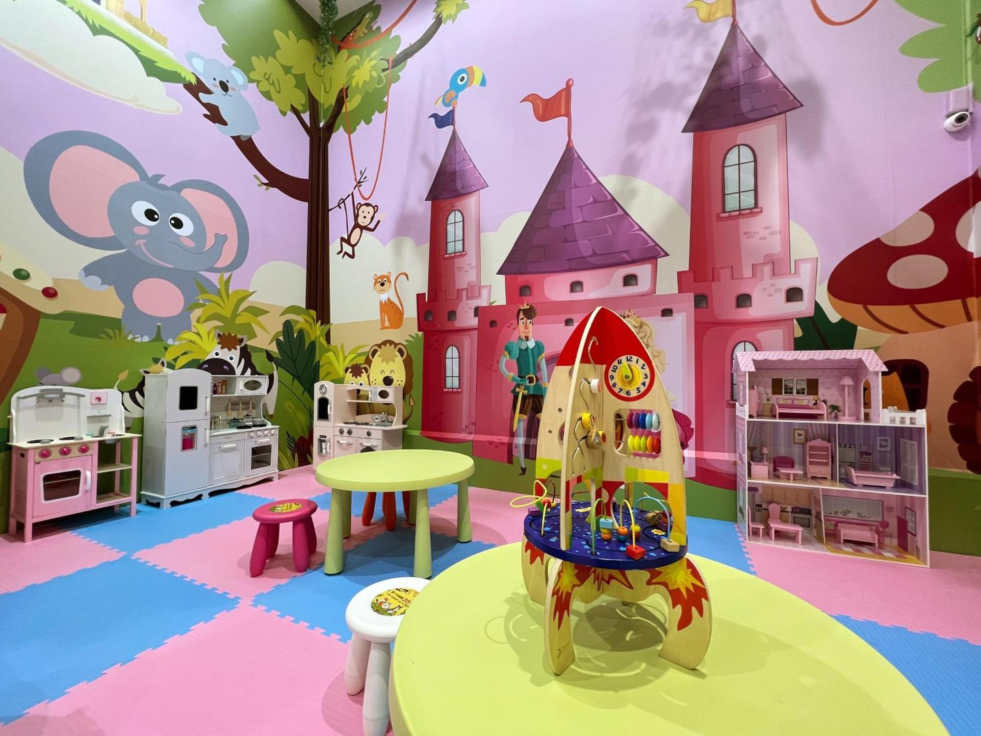 فندق إيفرجرين لوريل، تايتشونج تايتشونغ المظهر الخارجي الصورة The photo shows a colorful children's playroom designed with a whimsical theme. The walls are painted in bright colors and feature a cartoon-style mural of a pink castle with purple towers and a smiling cartoon elephant. The room is filled with playf