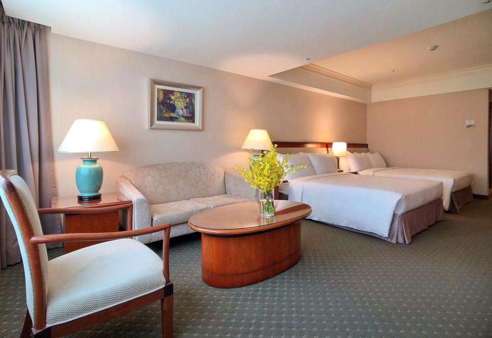 فندق إيفرجرين لوريل، تايتشونج تايتشونغ المظهر الخارجي الصورة The photo shows a hotel room featuring two beds, a small seating area, and a coffee table. The walls are painted in soft, neutral colors, and there is a framed piece of artwork hanging on the wall. A potted plant with yellow flowers is placed on the 