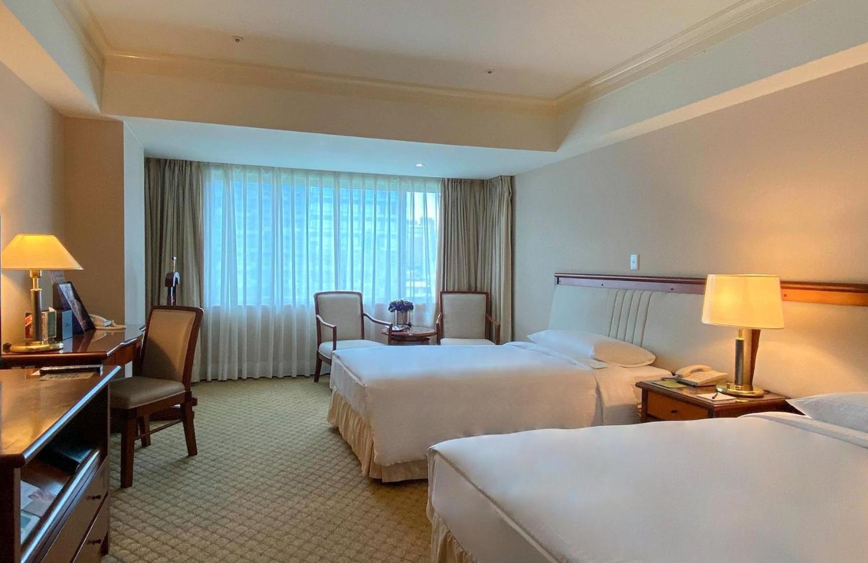 فندق إيفرجرين لوريل، تايتشونج تايتشونغ المظهر الخارجي الصورة The photo shows a hotel room featuring two single beds positioned near each other. There's a light-colored carpet on the floor and a large window with sheer curtains that allows natural light to fill the space. In the room, there are two chairs place