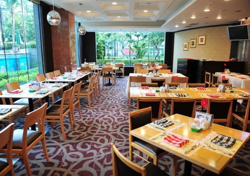 فندق إيفرجرين لوريل، تايتشونج تايتشونغ المظهر الخارجي الصورة The photo shows an interior of a restaurant with a spacious layout. There are several wooden tables, each set with napkins and utensils. The floor has a decorative carpet, and large windows provide a view of greenery outside. The lighting is bright, 