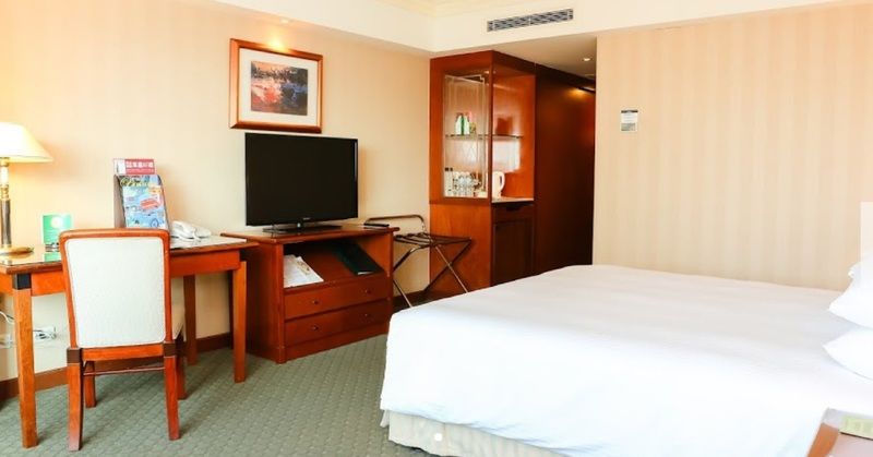 فندق إيفرجرين لوريل، تايتشونج تايتشونغ المظهر الخارجي الصورة The photo shows a hotel room featuring a neatly made bed with a white blanket. On one side, there is a wooden desk with a chair, and a flat-screen television is mounted nearby. An accent cabinet is visible, displaying various items. The walls are pai