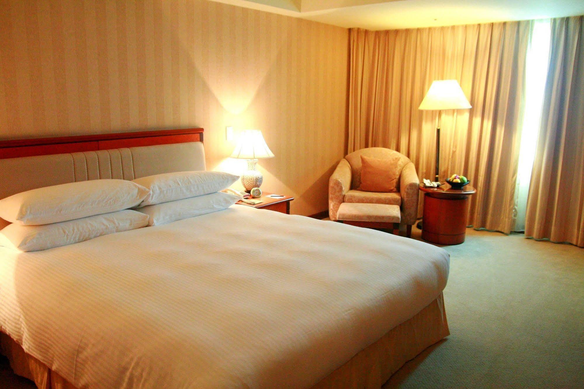 فندق إيفرجرين لوريل، تايتشونج تايتشونغ المظهر الخارجي الصورة The photo shows a hotel room containing a large bed with white linens, flanked by two bedside lamps. To one side, there is a cozy armchair and a small side table with a fruit bowl or snacks. The walls are decorated in a soft, neutral color, and there