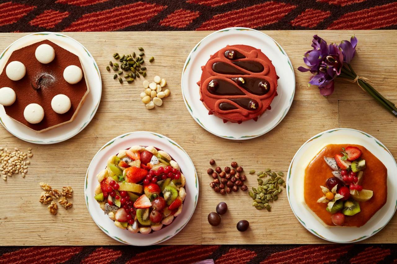 فندق إيفرجرين لوريل، تايتشونج تايتشونغ المظهر الخارجي الصورة The photo displays a variety of desserts arranged on small plates. There are three main cakes or tarts:

1. **Top Left Plate**: A round chocolate cake with a smooth surface and white decorations on top.
2. **Top Middle Plate**: Another cake, possibly