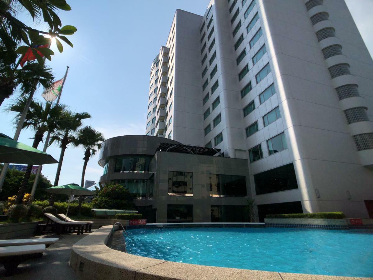 فندق إيفرجرين لوريل، تايتشونج تايتشونغ المظهر الخارجي الصورة The photo depicts a hotel or residential building alongside a swimming pool. The pool is situated in the foreground, with a curved section of the building visible behind it. Surrounding the pool, there are lounge chairs for relaxation. In the backgro