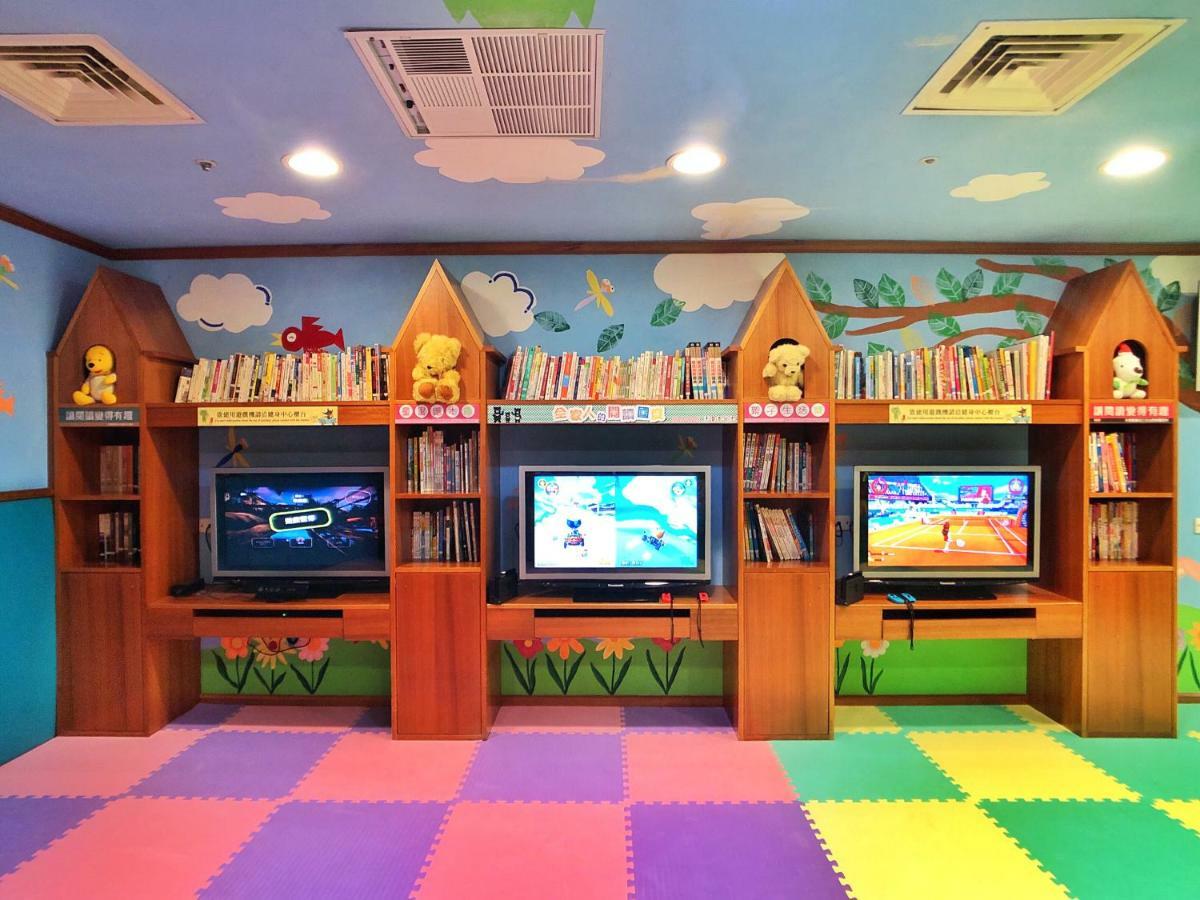 فندق إيفرجرين لوريل، تايتشونج تايتشونغ المظهر الخارجي الصورة The photo shows a colorful and playful room designed for children. In the center, there are three wooden gaming stations, each equipped with a television screen and surrounded by shelves filled with books. The walls are decorated with cheerful images