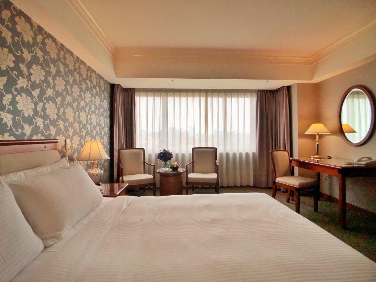 فندق إيفرجرين لوريل، تايتشونج تايتشونغ المظهر الخارجي الصورة The photo shows a hotel room with a comfortable and inviting design. There is a large bed with crisp white bedding on the left side of the image. To the right, there are two elegant chairs with a small round table between them, adorned with a bouquet
