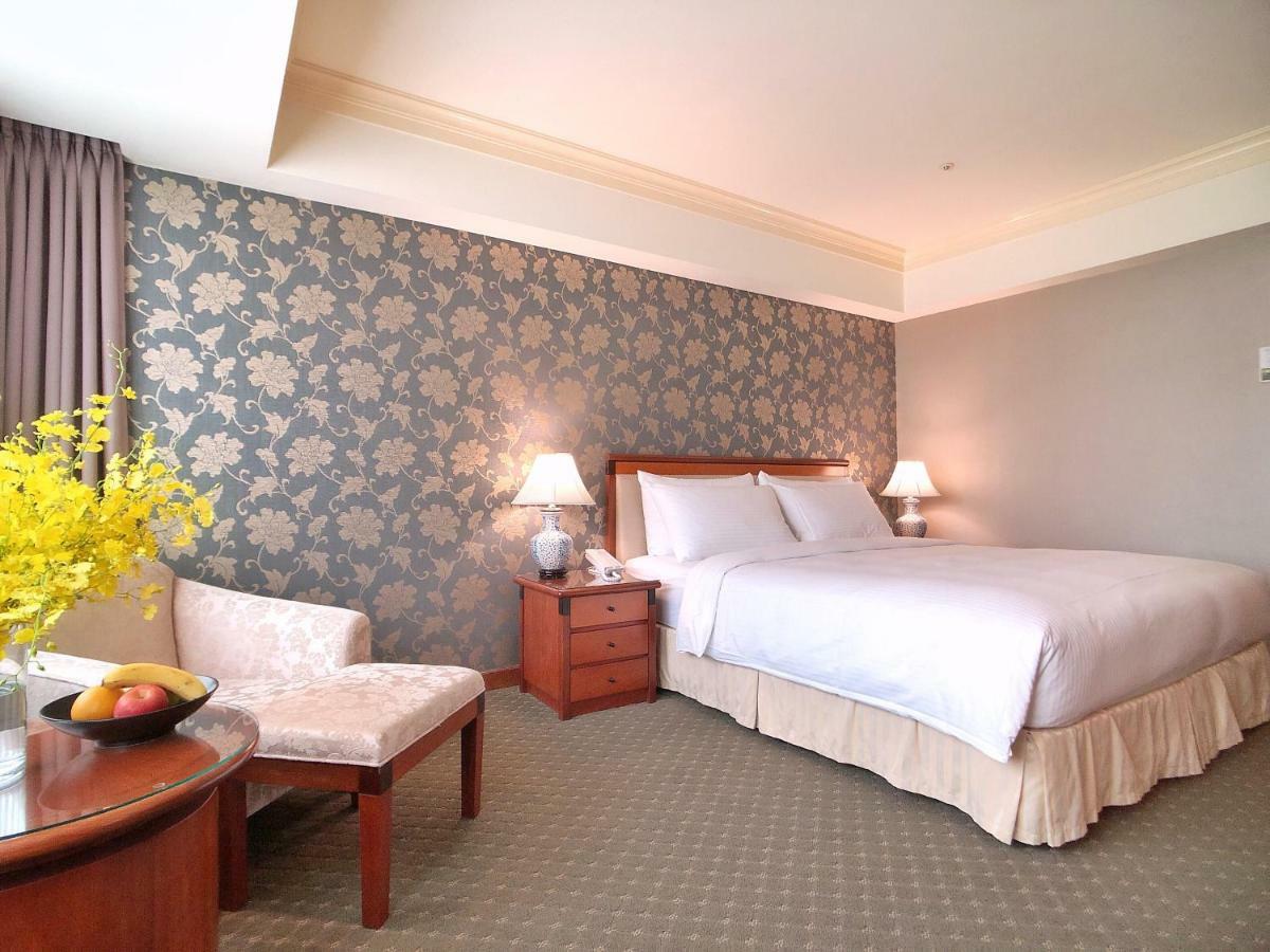 فندق إيفرجرين لوريل، تايتشونج تايتشونغ المظهر الخارجي الصورة The photo shows a well-decorated hotel room. It features a large bed with white bedding, situated against a patterned wall with floral designs. On either side of the bed are bedside tables with lamps. There is a small seating area that includes a cha