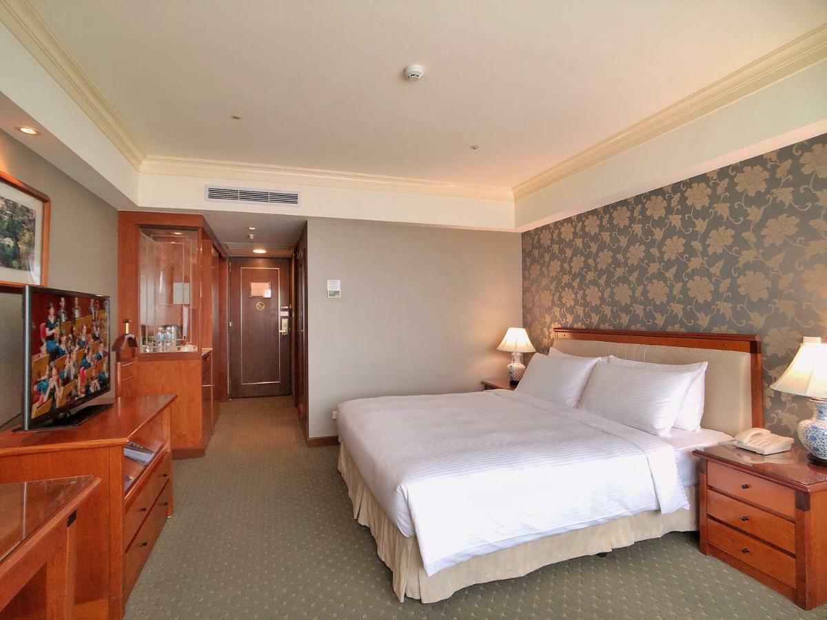 فندق إيفرجرين لوريل، تايتشونج تايتشونغ المظهر الخارجي الصورة The photo shows a well-furnished hotel room. It features a large bed with white linens positioned against a decorative wall. On either side of the bed are bedside tables with lamps. There’s a television mounted on a wooden cabinet across from the bed