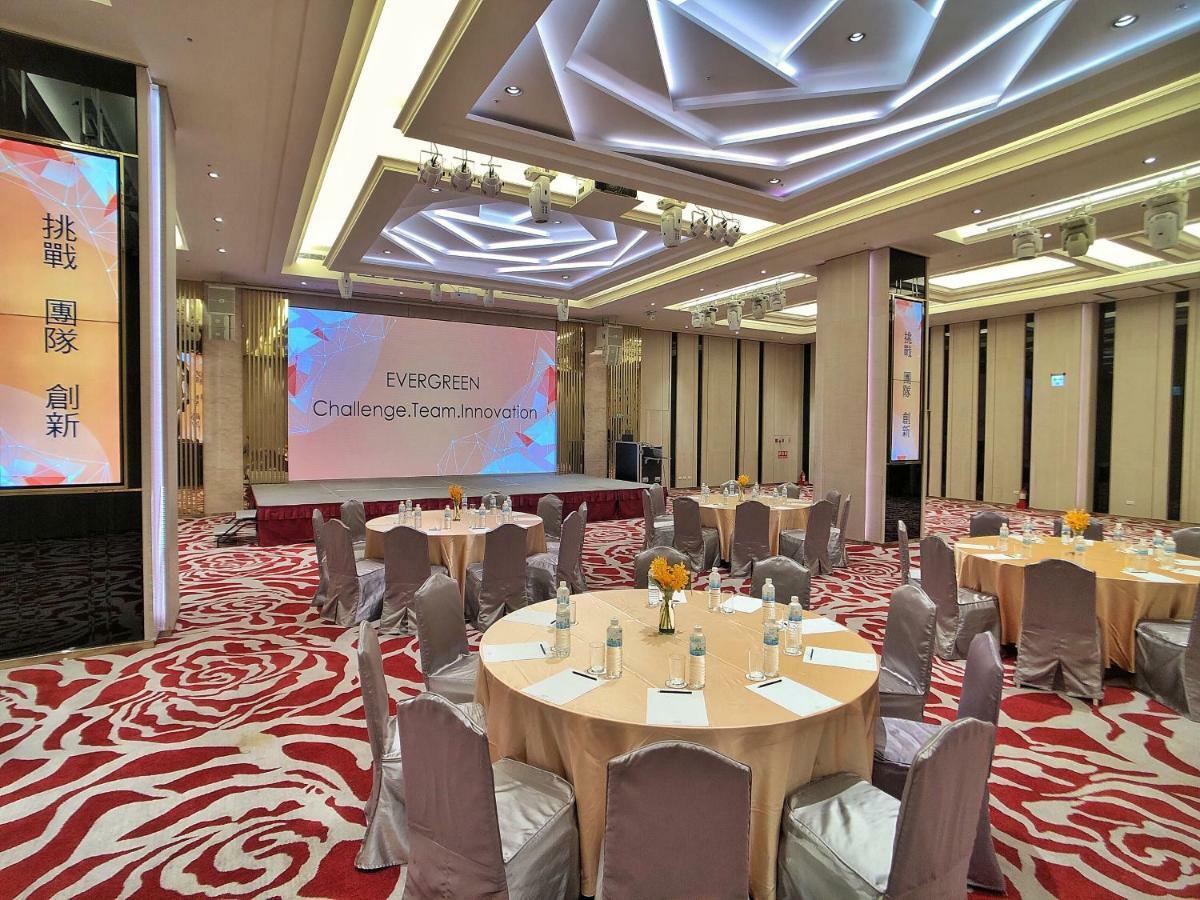 فندق إيفرجرين لوريل، تايتشونج تايتشونغ المظهر الخارجي الصورة The photo shows a conference or event space set up for a gathering. The room features several round tables with light-colored tablecloths and chairs, each with decoration, possibly for dining or discussion. A large screen displays the text "EVERGREEN