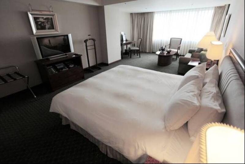 فندق إيفرجرين لوريل، تايتشونج تايتشونغ المظهر الخارجي الصورة The photo shows a hotel room featuring a large bed with white bedding. There is a flat-screen television on a wooden cabinet opposite the bed. Nearby, there are two armchairs and a small table, creating a cozy seating area. Large windows allow natura