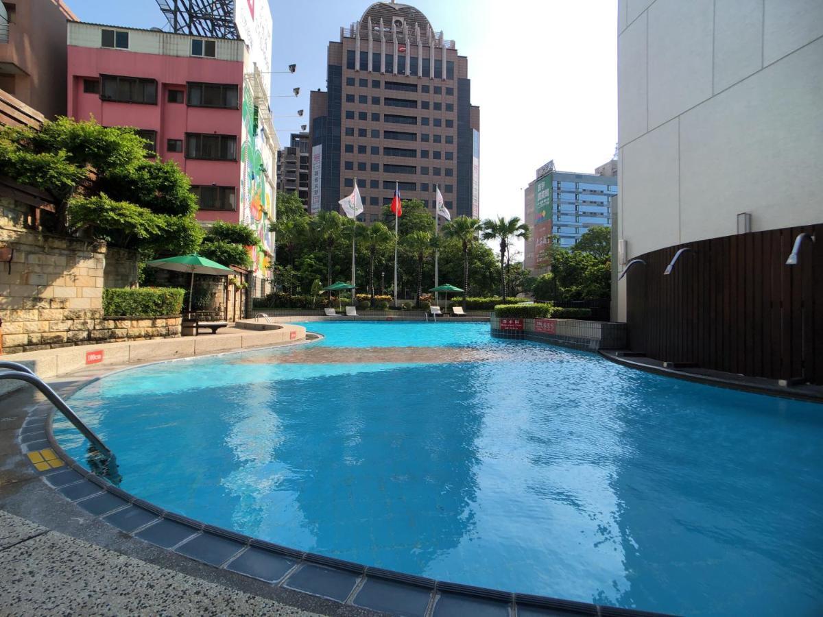فندق إيفرجرين لوريل، تايتشونج تايتشونغ المظهر الخارجي الصورة The photo shows a swimming pool area set in an outdoor environment. The pool has a clear blue water and a gently curving shape. Surrounding the pool are some green trees and plants, along with a few umbrellas providing shade. In the background, there